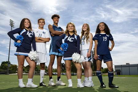 Eine Gruppe von Cheerleadern der Linfield Christian School steht gemeinsam auf einem grasbewachsenen Feld unter bewölktem Himmel.