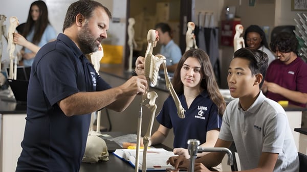 Ein Mann steht vor einer Gruppe Schüler der Linfield Christian School und hält ein Skelettmodell während des Anatomieunterrichts.