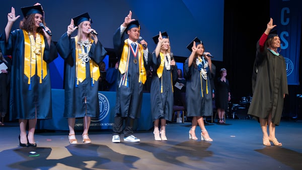 Absolventen der Linfield Christian School stehen auf einer Bühne und feiern ihre Graduierung in gelben und schwarzen Talaren.