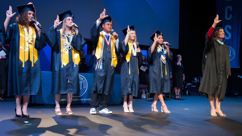 Absolventen der Linfield Christian School stehen auf einer Bühne und feiern ihre Graduierung in gelben und schwarzen Talaren.
