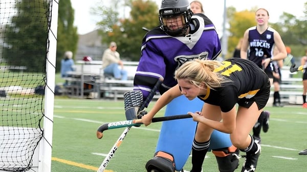 Eine Spielerin der Listowel District Secondary School im lila Trikot spielt Hockey vor dem Tor.