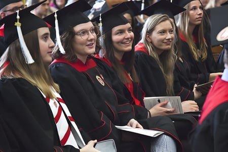 Eine Gruppe von Absolventen der Listowel District Secondary School in schwarzen und roten Talaren hält stolz ihre Diplome.