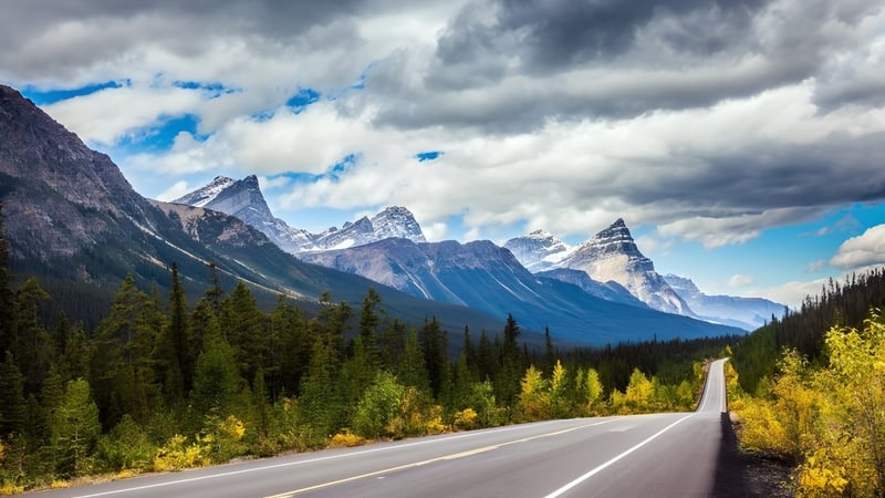 Eine gewundene Straße führt durch ein bewaldetes Tal mit schneebedeckten Bergen im Hintergrund nahe der Listowel District Secondary School.