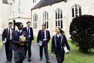 Eine Gruppe Schüler in Schuluniform geht gemeinsam auf dem Hof von Llandovery College mit gotischer Architektur.