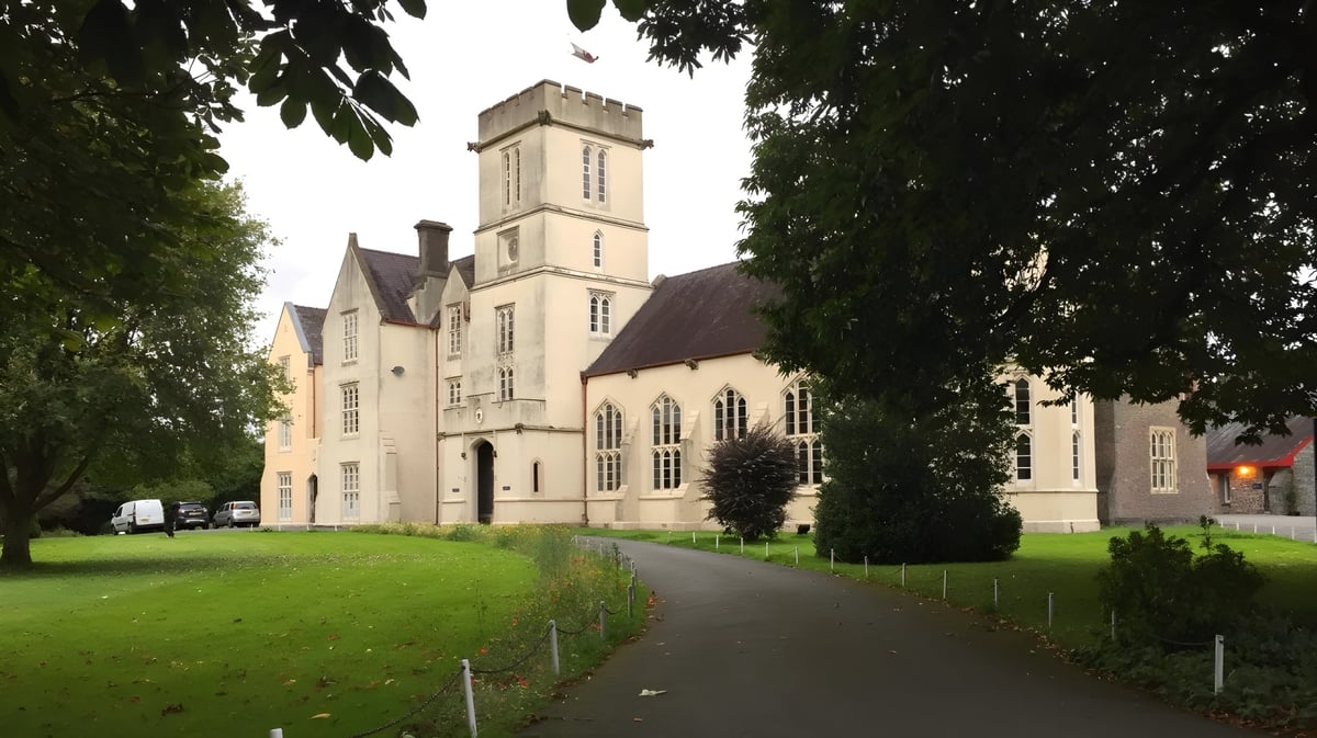 Das mittelalterliche Hauptgebäude mit hohem Turm auf dem Campus des Llandovery College ist von grüner Landschaft umgeben.