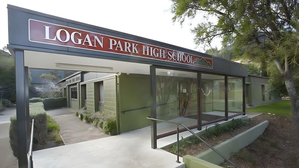 Die Außenansicht von Logan Park High School mit beschildertem Eingang und gestalteter Grünanlage im Vordergrund.