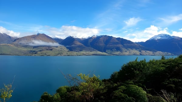 Ein türkisfarbener See liegt vor schneebedeckten Bergen, die von üppigem Grün umgeben sind.