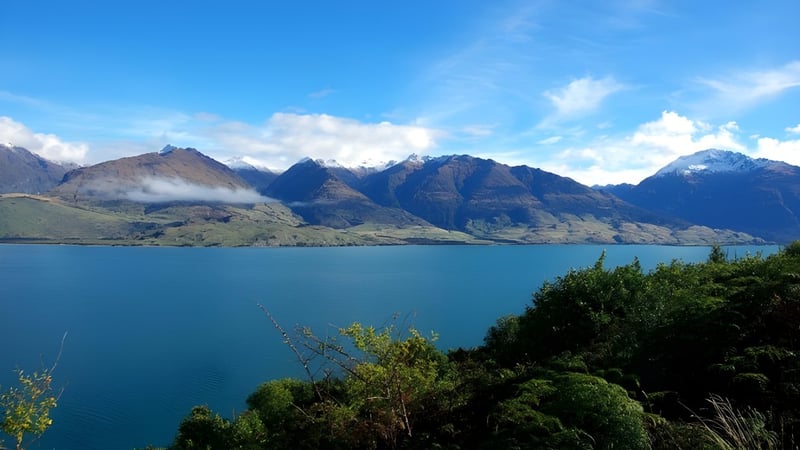 Ein türkisfarbener See liegt vor schneebedeckten Bergen, die von üppigem Grün umgeben sind.