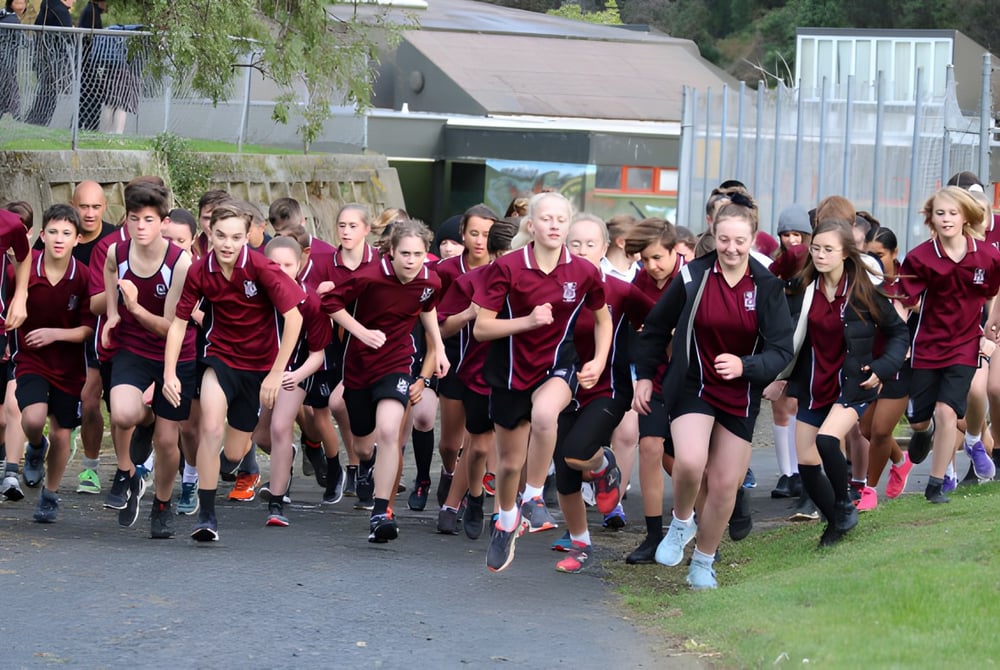 Schüler der Logan Park High School laufen in einheitlicher Kleidung gemeinsam auf einem Weg entlang von Grünflächen und Gebäuden.