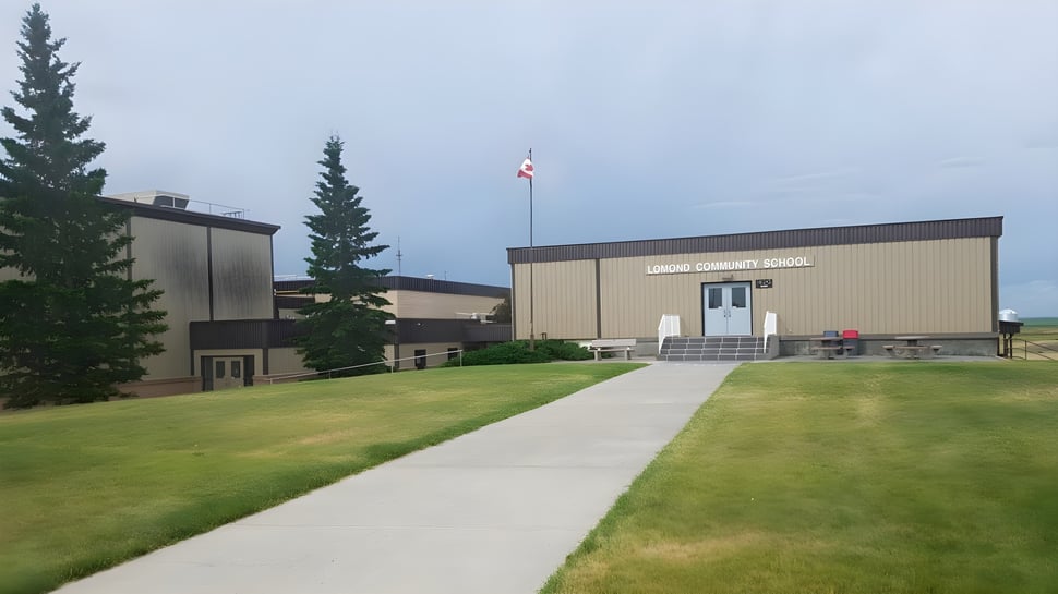 Das moderne Gebäude der Lomond Community School mit kanadischer Flagge ist von Rasen und hohen Kiefern umgeben.