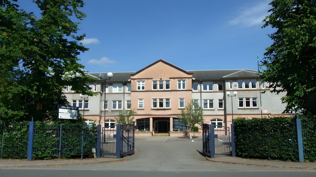 Das mehrstöckige Backsteingebäude der Lomond School mit Satteldach wird von grüner Umgebung und einem gepflasterten Weg mit Toren im Vordergrund umgeben.