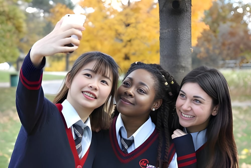 Drei Schülerinnen der London International Academy machen im herbstlichen Park zusammen ein Selfie.