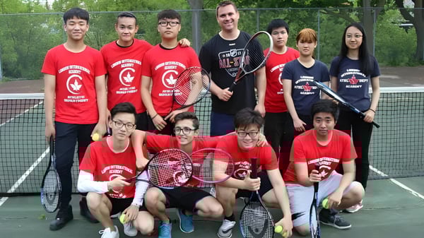 Eine Gruppe von Schülern der London International Academy posiert gemeinsam auf einem Tennisplatz in roten Shirts.