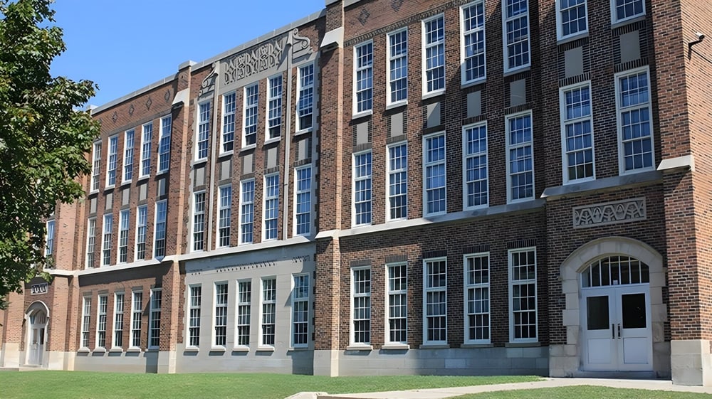 Das mehrstöckige Backsteingebäude mit vielen Fenstern und einem gewölbten Eingang des London South Collegiate Institute ist von Bäumen umgeben.