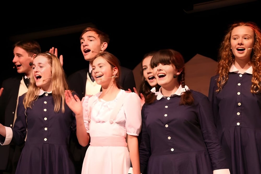 Eine Gruppe Schülerinnen der Long Bay College führt auf der Bühne in dunkler Kleidung unter dramatischer Beleuchtung auf.