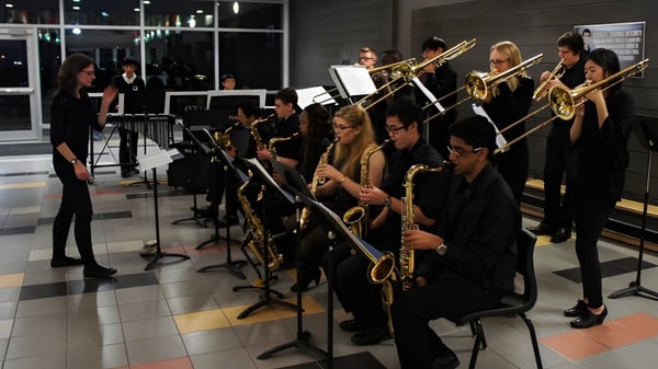 Eine Gruppe Musiker der Longfields-Davidson Heights Secondary School tritt in schwarzer Kleidung auf einer Bühne mit gedämpfter Beleuchtung auf.