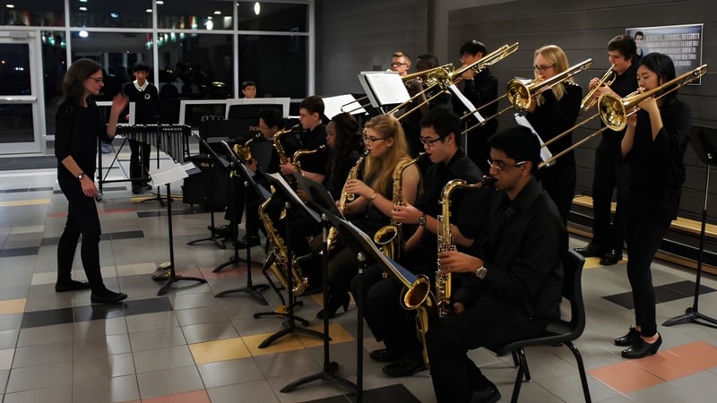 Eine Gruppe Musiker der Longfields-Davidson Heights Secondary School tritt in schwarzer Kleidung auf einer Bühne mit gedämpfter Beleuchtung auf.