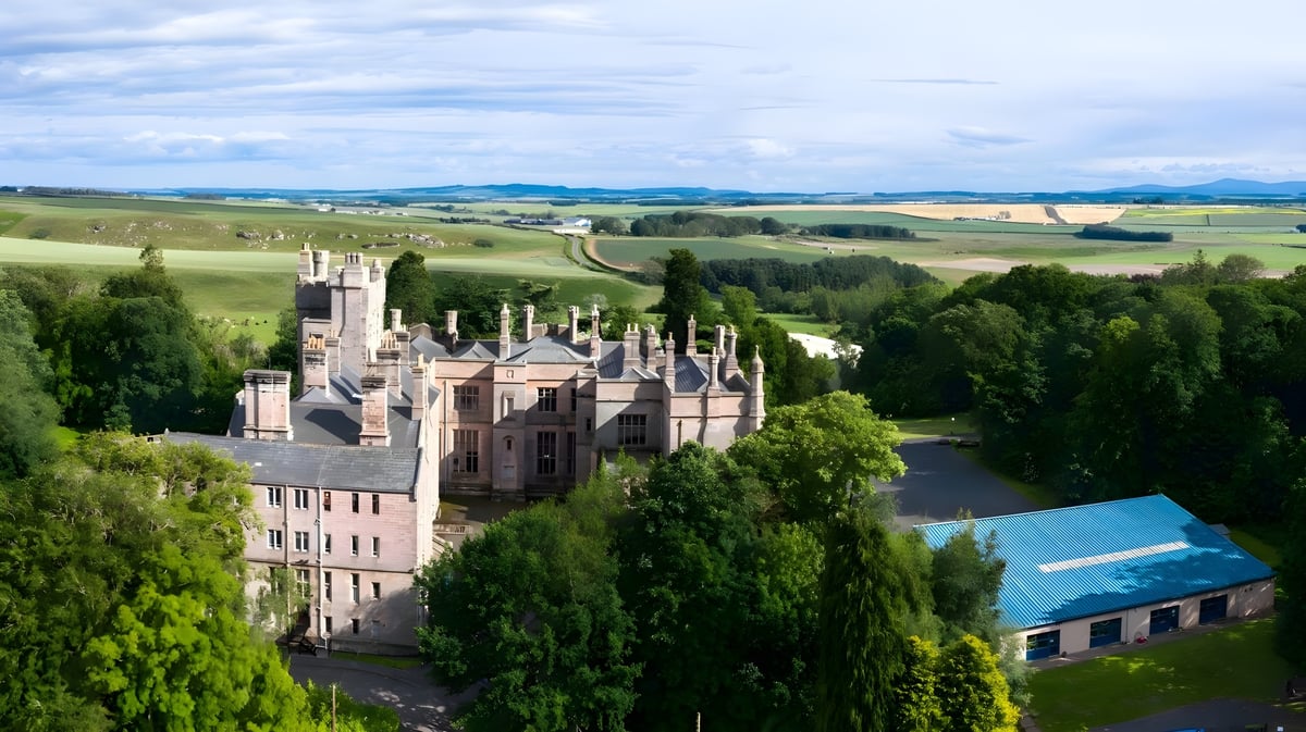 Ein mittelalterlich anmutendes Schloss umgeben von Hügeln und Waldlandschaften auf dem Gelände der Longridge Towers School.