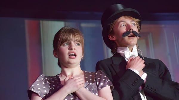 Eine Frau mit überraschter Miene und ein Mann mit Schnurrbart stehen in einem schwach beleuchteten Raum der Longridge Towers School.