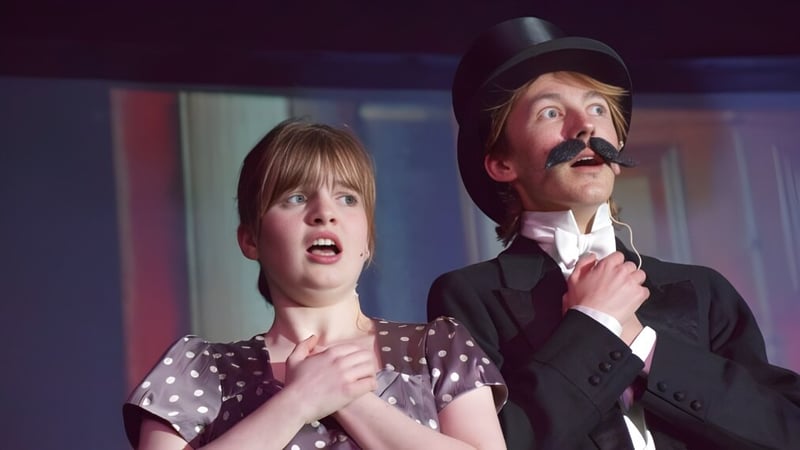 Eine Frau mit überraschter Miene und ein Mann mit Schnurrbart stehen in einem schwach beleuchteten Raum der Longridge Towers School.