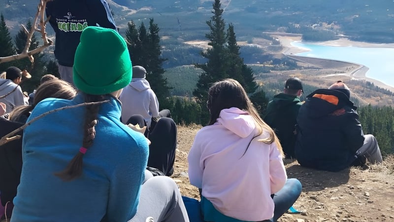 Eine Gruppe von Schülern der Lord Beaverbrook High School steht auf einem Hügel und blickt auf eine Berglandschaft mit einer Straße.