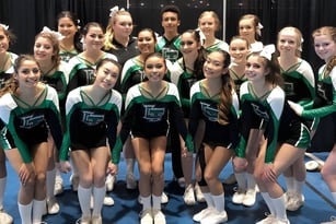 Eine Gruppe junger Gymnastinnen der Lord Tweedsmuir Secondary School posiert gemeinsam in grünen und schwarzen Uniformen auf einer Bühne.