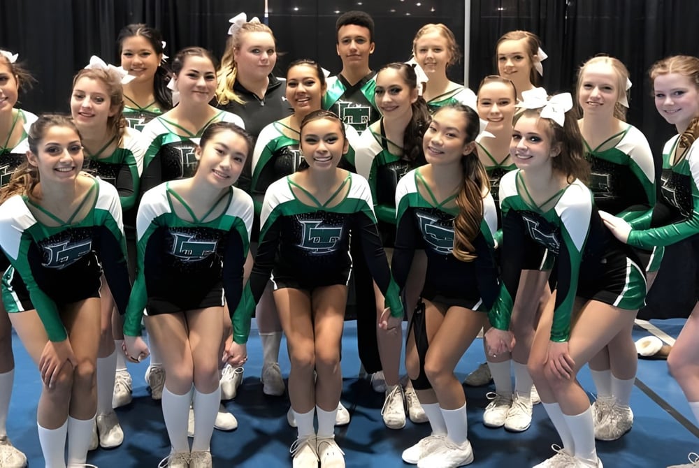 Eine Gruppe junger Gymnastinnen der Lord Tweedsmuir Secondary School posiert gemeinsam in grünen und schwarzen Uniformen auf einer Bühne.