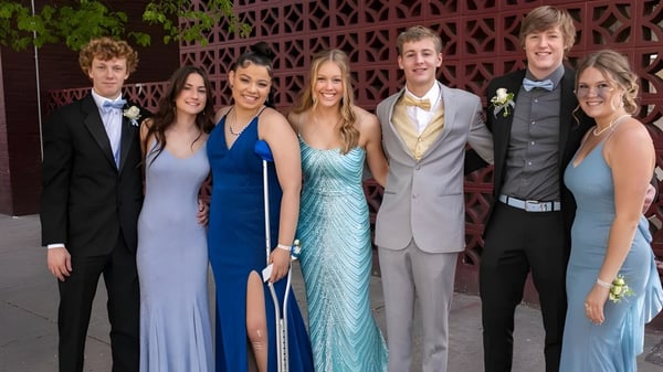 Eine Gruppe gut gekleideter Personen posiert vor einer dekorativen Gitterstruktur auf dem Gelände der Lord Tweedsmuir Secondary School.