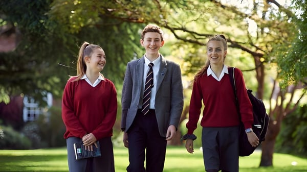 Drei Schüler des Lord Wandsworth College gehen gemeinsam auf einem grasbewachsenen Weg zwischen Bäumen auf dem Campus.