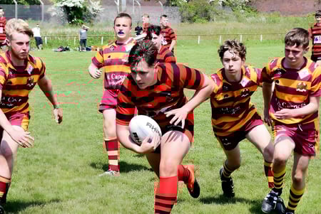 Schüler des Lord Wandsworth College spielen Rugby auf einem Spielfeld vor Zuschauern und Gebäuden.