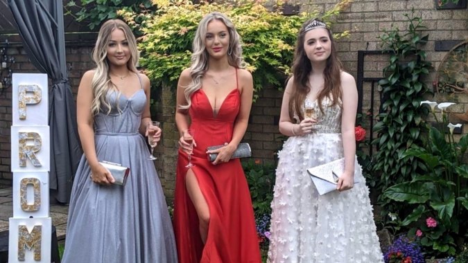 Drei Schülerinnen in formeller Kleidung stehen vor einem grünen Garten auf dem Gelände der Loreto Abbey Secondary School.