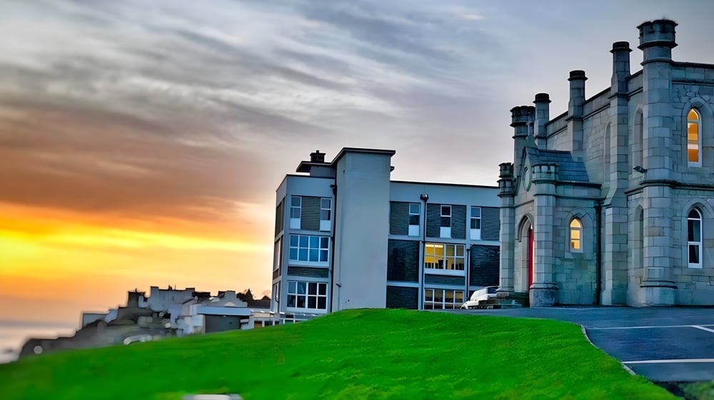 Ein historisches, schlossartiges Gebäude steht auf einem grünen Hügel bei Sonnenuntergang auf dem Campus der Loreto Abbey Secondary School.