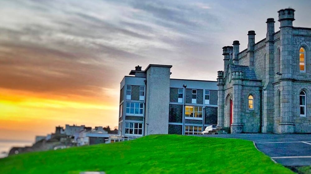 Das Schlossähnliche Gebäude der Loreto Abbey Secondary School steht auf einem grasbewachsenen Hügel vor einem Sonnenuntergang.