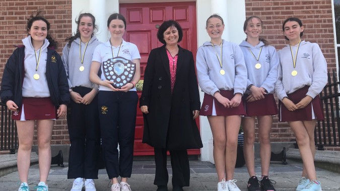 Eine Gruppe junger Frauen in Sportkleidung mit Medaillen steht vor einem Backsteingebäude auf dem Campus des Loreto College, St. Stephen's Green.