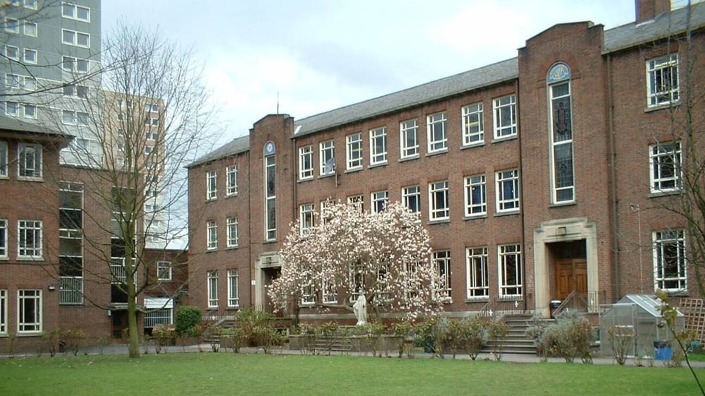 Das mehrstöckige Backsteingebäude des Loreto College Cavan ist von einer grünen Wiese und einem blühenden Baum umgeben.