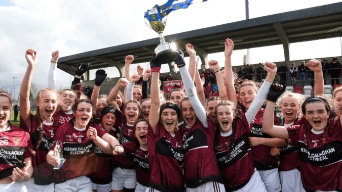 Schülerinnen des Loreto College Cavan feiern mit Pokal im Sportstadion im Hintergrund.
