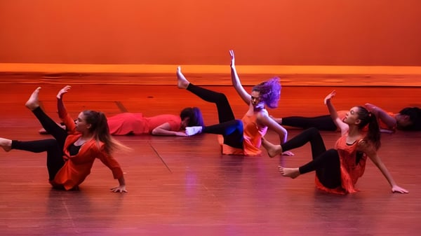 Eine Gruppe von Schülerinnen und Schülern des Loreto College Cavan führt eine Tanzaufführung vor orangem Bühnenhintergrund auf.