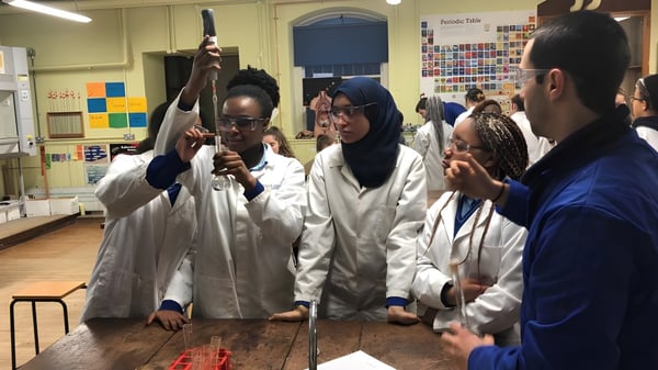 Schülerinnen und Schüler des Loreto College Mullingar arbeiten in weißen Laborkitteln in einem Klassenraum mit wissenschaftlichen Materialien.