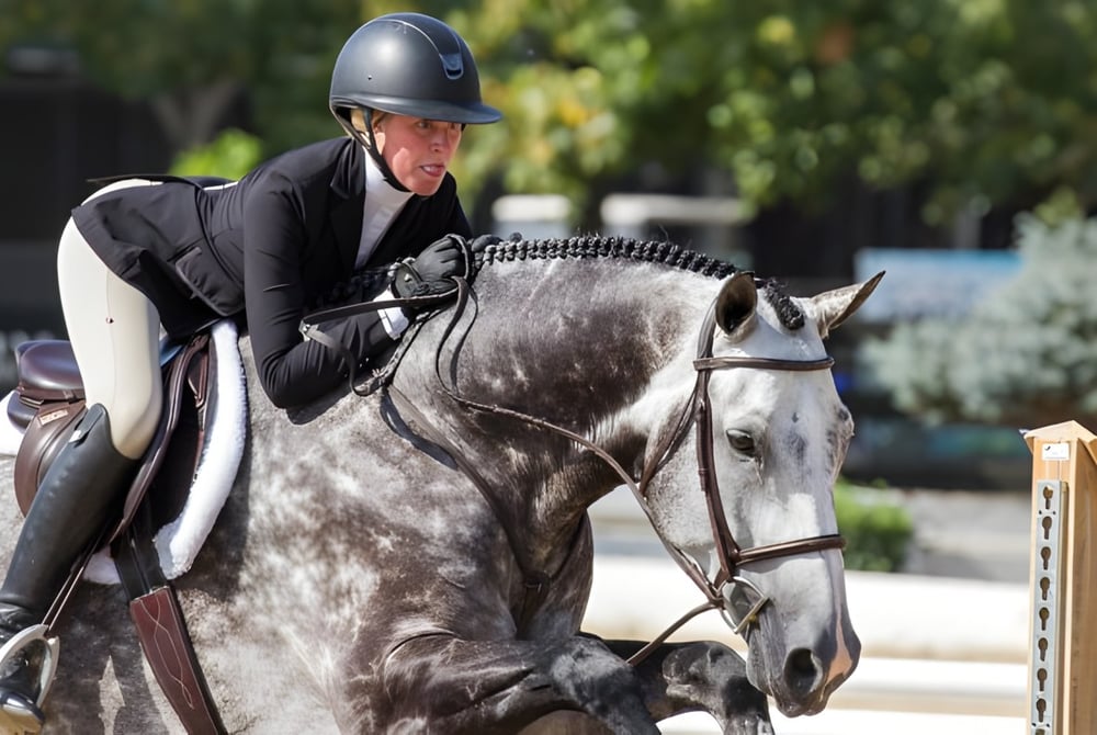 Eine Schülerin des Loreto College Mullingar reitet auf einem grauen Pferd im Freien.