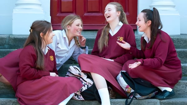Schülerinnen des Loreto College, St. Stephen's Green, stehen lachend in roten Roben vor einer roten Holztür.
