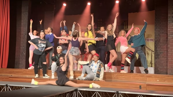 Schülerinnen und Schüler der Loreto High School Beaufort stehen auf der Bühne während einer Aufführung mit bunter Beleuchtung.