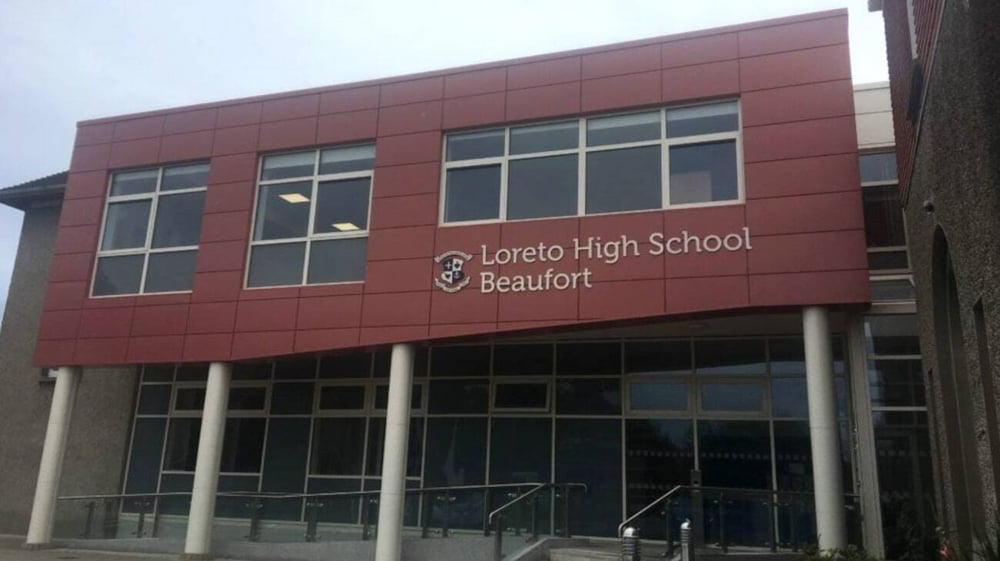 Das rote Hauptgebäude der Loreto High School Beaufort mit dem Schriftzug auf der Fassade ist von einem gepflasterten Bereich umgeben.