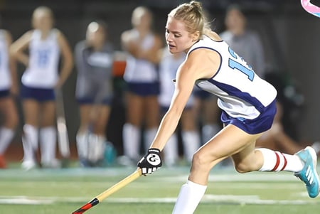 Eine Athletin der Loreto High School Beaufort läuft auf einem Sportfeld mit weiteren Athletinnen im Hintergrund.