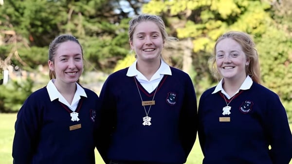 Drei Schülerinnen der Loreto High School Beaufort stehen lächelnd in einem parkähnlichen Bereich mit Bäumen und Grünflächen.