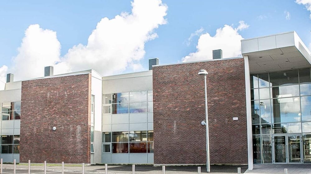 Das moderne mehrstöckige Gebäude der Loreto Secondary School mit Backsteinfassade und großen Glasfenstern bei bewölktem Himmel.
