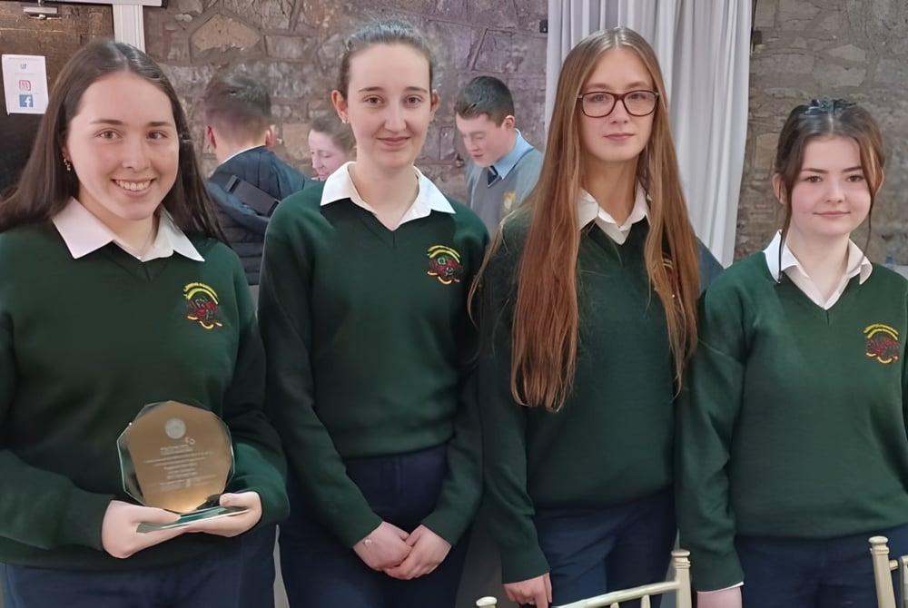 Eine Gruppe Schülerinnen und Schüler in grüner Schuluniform steht vor einem steinernen Gebäude auf dem Campus der Loreto Secondary School in Cork.