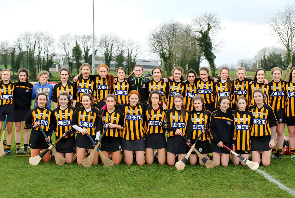 Eine große Gruppe junger Sportlerinnen steht auf dem Rasen der Loreto Secondary School vor Bäumen und Gebäuden.