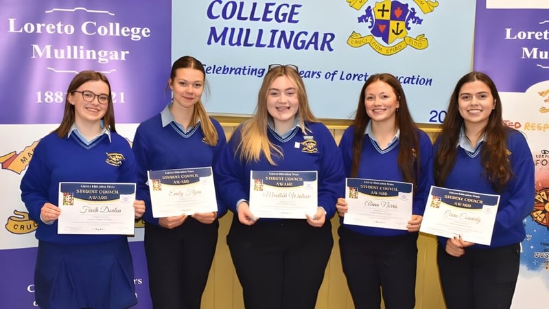 Fünf Schülerinnen des Loreto College Mullingar präsentieren stolz ihre Zertifikate vor einem Banner der Schule.