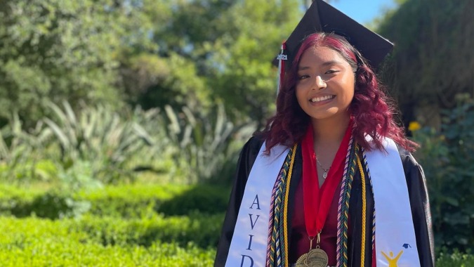 Eine junge Frau in Abschlusskleidung steht im grünen Außenbereich des Los Angeles Unified School District.