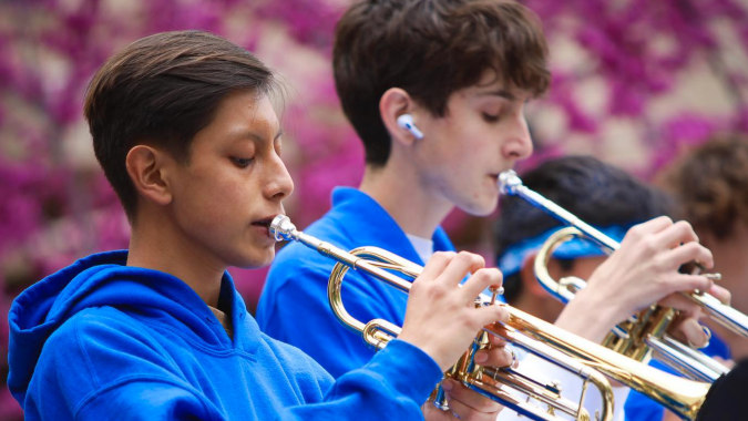 Zwei Schüler im Los Angeles Unified School District spielen Blechblasinstrumente vor lilafarbenen Blumen.
